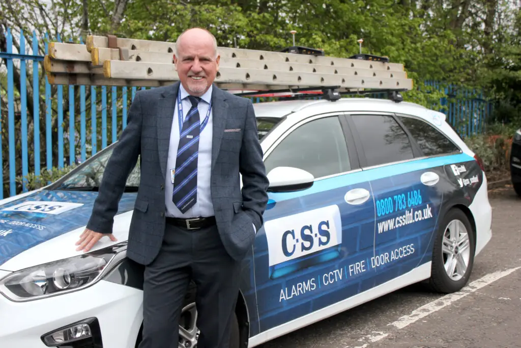 Photo of Paul Connelly standing smiling and resting his right hand on the bonnet of a CSS branded car.