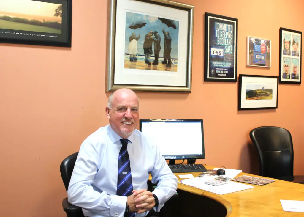 Paul Connelly smiling and sitting at the desk in his office in front of a PC.