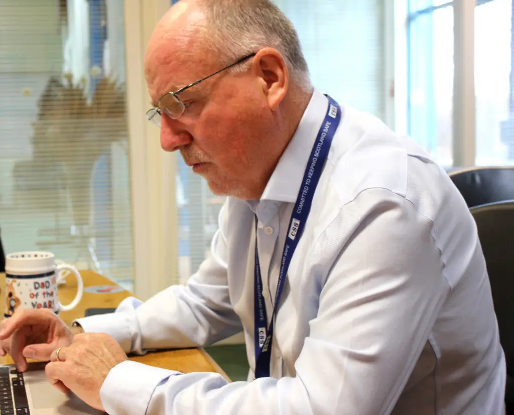 Paul Connelly working at PC; a mug on his desk has an image of a teddy bear on it and text reads dad of the year.