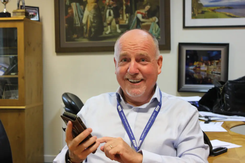 Paul Connelly looking amusedly at the camer and dialling a mobile phone.