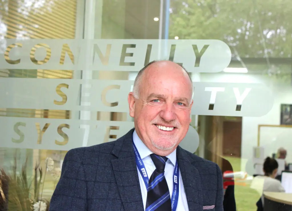 Photo of Paul Connelly smiling and standing in front of a glass door that says Connelly Security Systems.