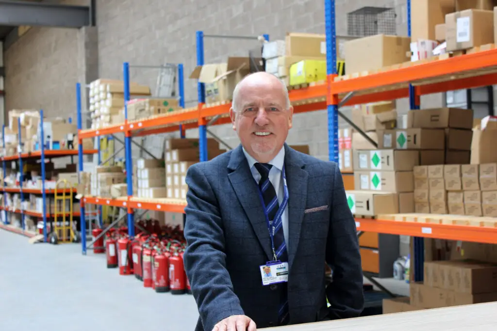 Photo of Paul Connelly smiling and standing in a warehouse. Shelves and boxes are visible behind him.