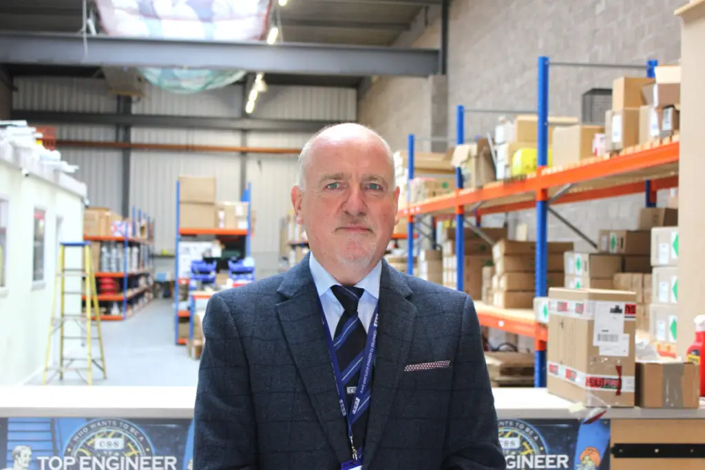 Photo of Paul Connelly standing in front of a counter in a warehouse. Shelves and boxes are visible behind him.