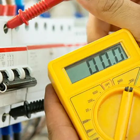 Image of yellow electronic device with dial pointing to 200 and LCD display which reads 00.0. A thumb and forefinger hold a red plastic connector to a hole in a fuse box.