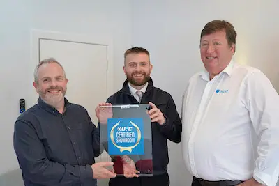 Photo shows three men standing in a row with two men holding the IDES URC Certified showroom certification in a clear presentation sleeve.