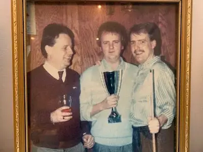 Photo of Paul Connelly, CEO Connelly Group Holdings, with his two brothers Jim and Pat. The man on the left holds a pint of beer, the man in the middle holds a trophy and the man on the right holds an upright snooker cue.