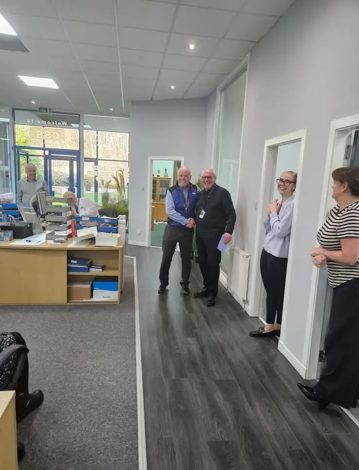 Paul Connelly shaking hands with John McDaid as coworkers look on smiling - css celebrates john mcdaid work anniversary